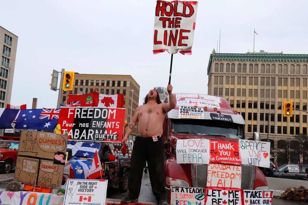 Uma pessoa segura uma placa na frente de caminhões bloqueando uma rua do centro enquanto motoristas de caminhão e seus apoiadores continuam protestando contra os mandatos de uma vacina contra o coronavírus (COVID-19) em Ottawa, Ontário, Canadá.