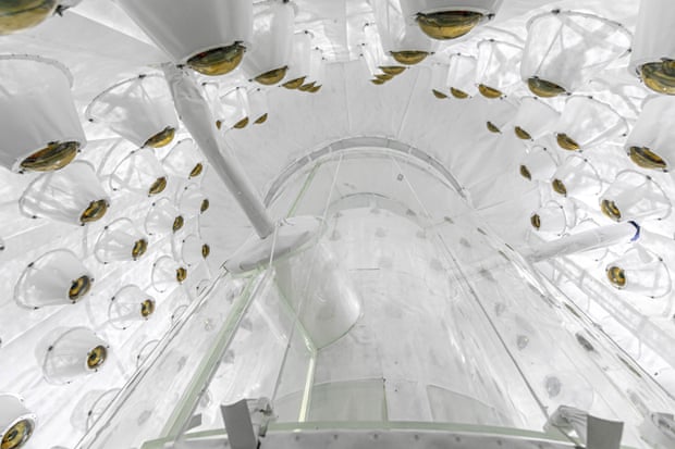 Uma câmara toda branca, vista de um ângulo baixo, forrada com ferragens em forma de cúpula, todas voltadas para um cilindro transparente.