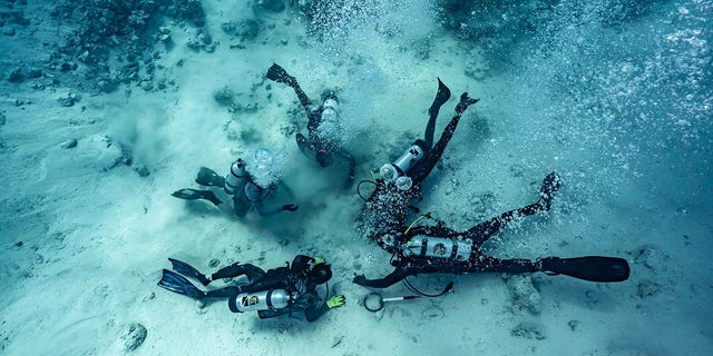 Mergulhadores são mostrados cavando tesouros enterrados no fundo do mar - o local de um naufrágio nas Bahamas.