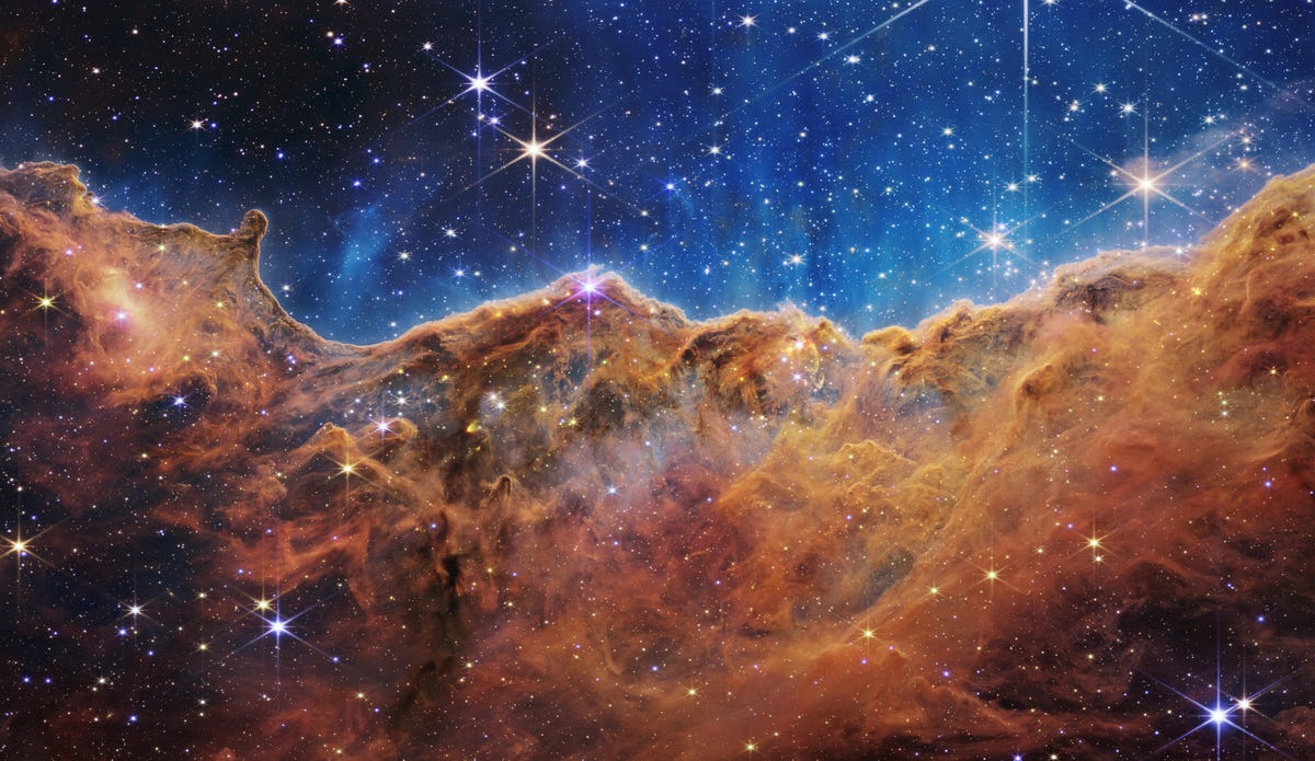 A Nebulosa Carina: Estrelas brilham contra um fundo índigo acima de nuvens de gás bronze enferrujado