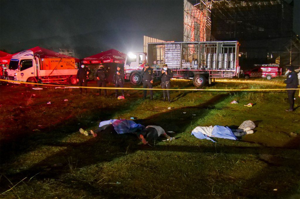 Bombeiros e policiais estão ao lado dos corpos de pessoas que morreram em uma debandada durante um show ao ar livre para comemorar o Dia da Independência em Quetzaltenango, Guatemala,