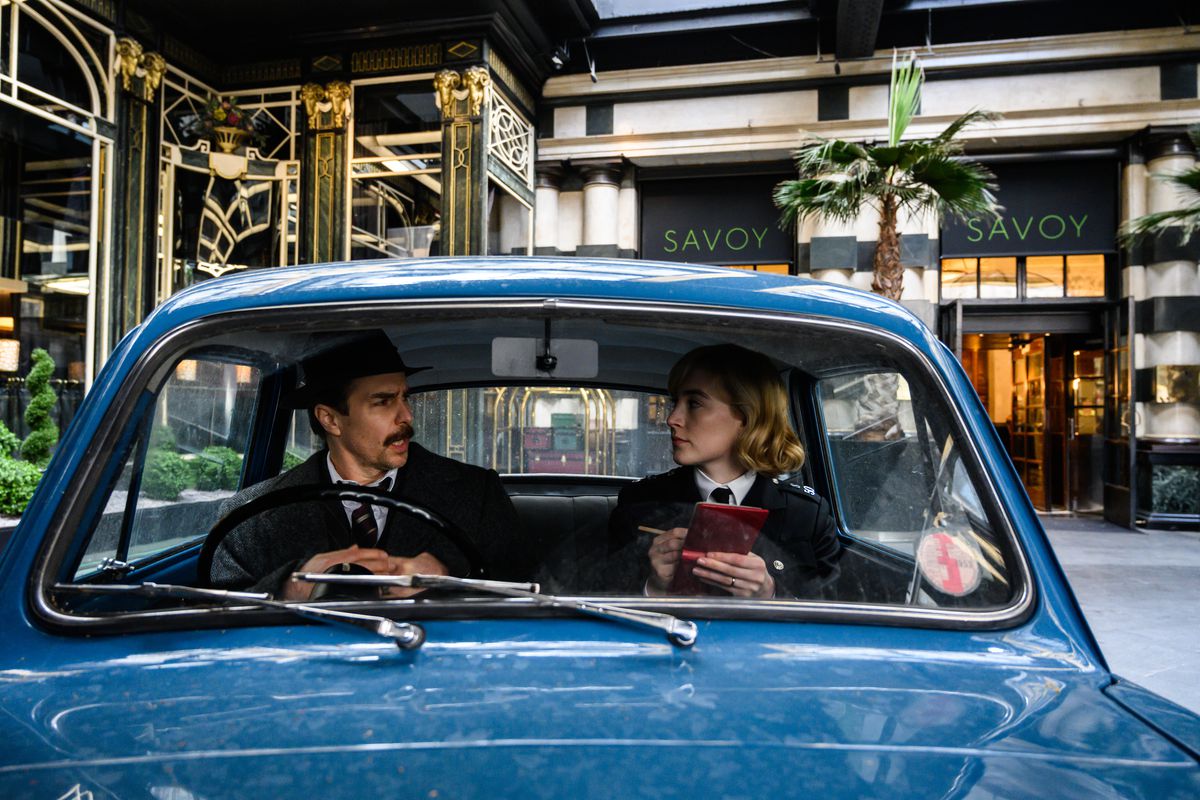 Inspetor Stoppard (Sam Rockwell) e Constable Stalker (Saoirse Ronan) conversam em um pequeno carro azul da polícia do lado de fora do Savoy Hotel