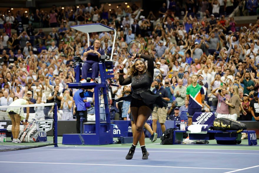 Serena Williams levanta sua raquete e braço para a multidão enquanto ela está na quadra após sua vitória